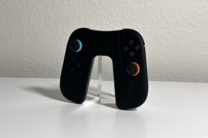 JSAUX Switch 2 charging grip holding a black pair of Joy-Con 2 with blue and orange stick rings, angled on a white desk