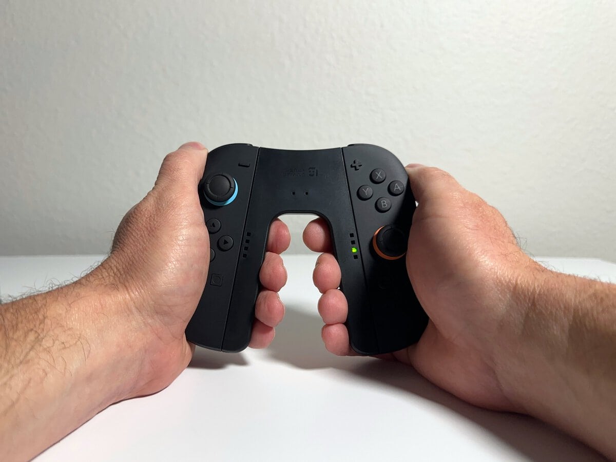 Two hands holding the JSAUX Switch 2 charging grip with both Joy-Con 2 attached, seen from the player's view