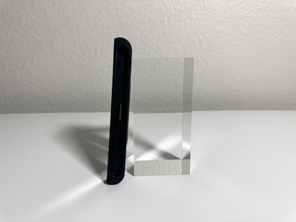 Side view of the JSAUX Switch 2 charging grip showing how thin it is next to a clear acrylic block