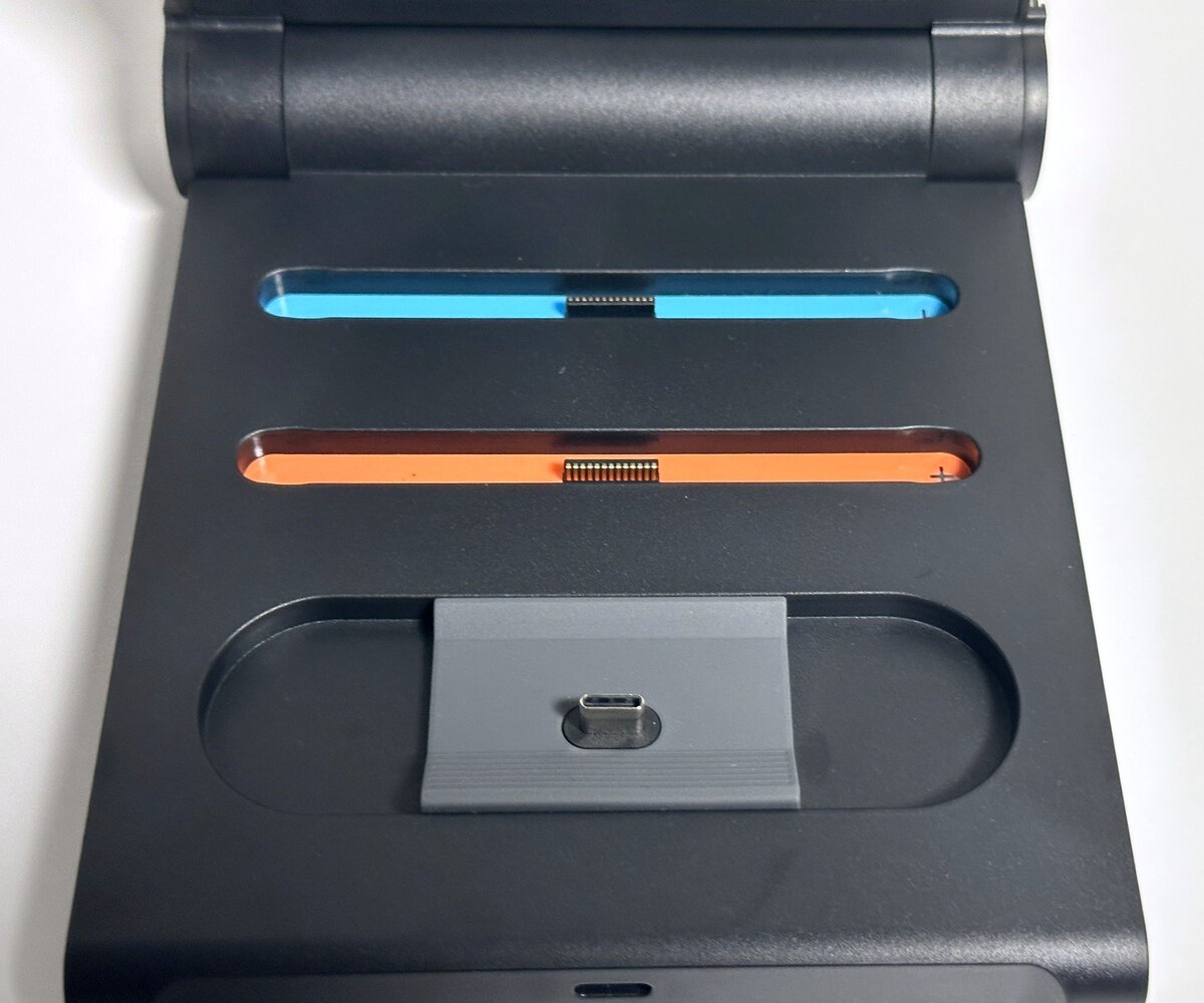 Top-down view of the switch 2 pro controller charging dock showing blue and orange color-coded Joy-Con 2 rails above the bare USB-C post for the Pro Controller