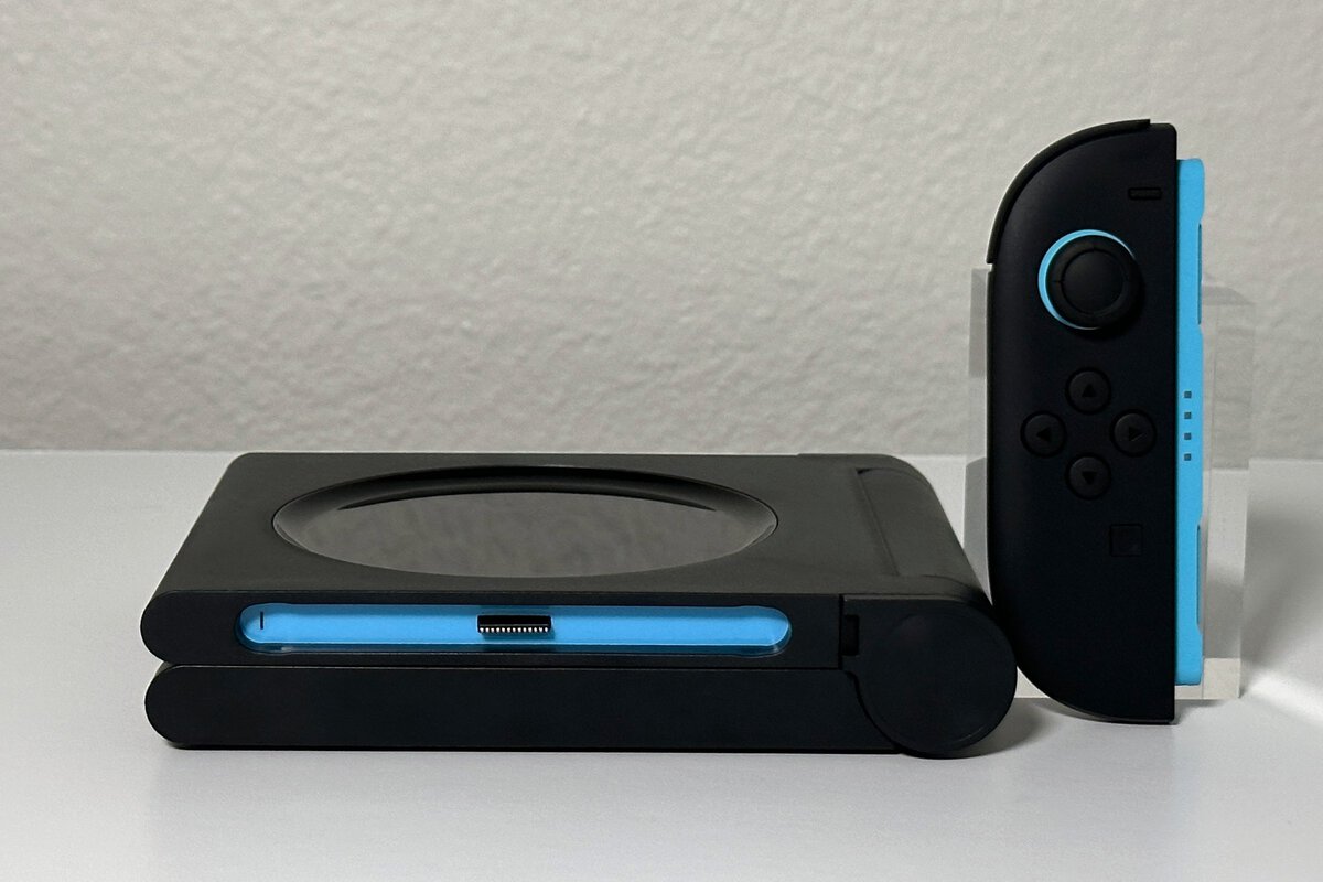 The switch 2 pro controller charging dock folded flat, with a blue-railed Joy-Con 2 standing beside it for scale
