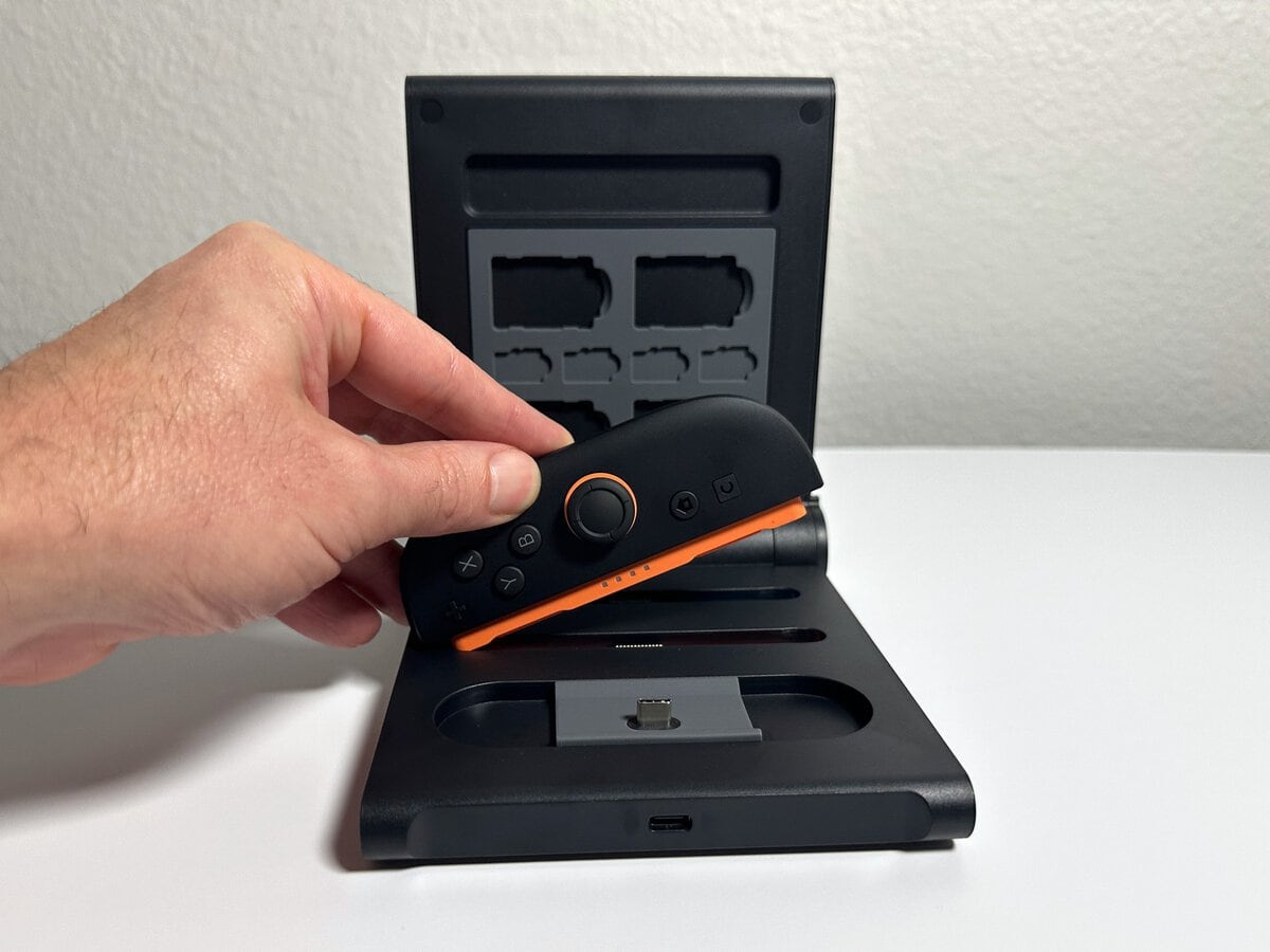 Hand lowering an orange-railed Joy-Con 2 into its slot on the JSAUX switch 2 pro controller charging dock