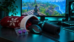 Stocking stuffers for gamers spilling from a red knit stocking on a teal-lit desk: a wired mouse, a rolled cloth mousepad and a pack of purple thumbstick caps